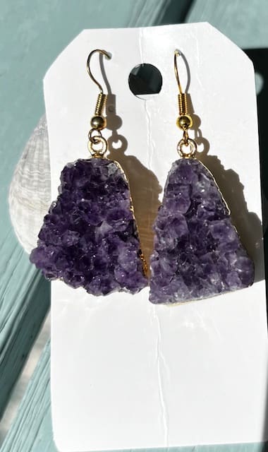 A pair of purple earrings hanging on top of a white card.